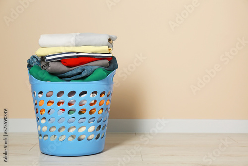 Plastic laundry basket with clean clothes on floor near beige wall. Space for text