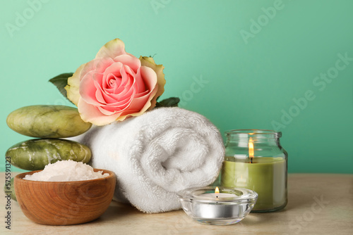 Composition with different spa products, candles and rose on beige table against turquoise background. Space for text