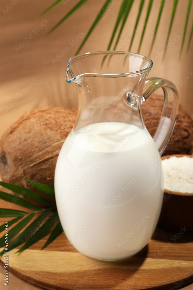 Glass jug of delicious vegan milk near coconuts on brown background Glass jug of delicious vegan milk near coconuts on brown background