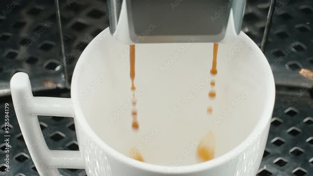 The white cup filling up a coffee from the machine inside the kitchen in Estonia The white cup filling up a coffee from the machine inside the kitchen in Estonia