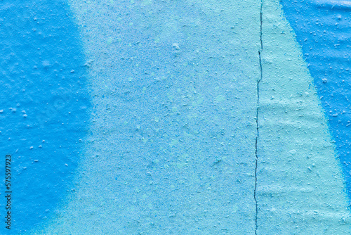 Macro close-up of a cracked wall spray painted in light blue and turquoise. Abstract full frame textured splattered graffiti background with copy space.
