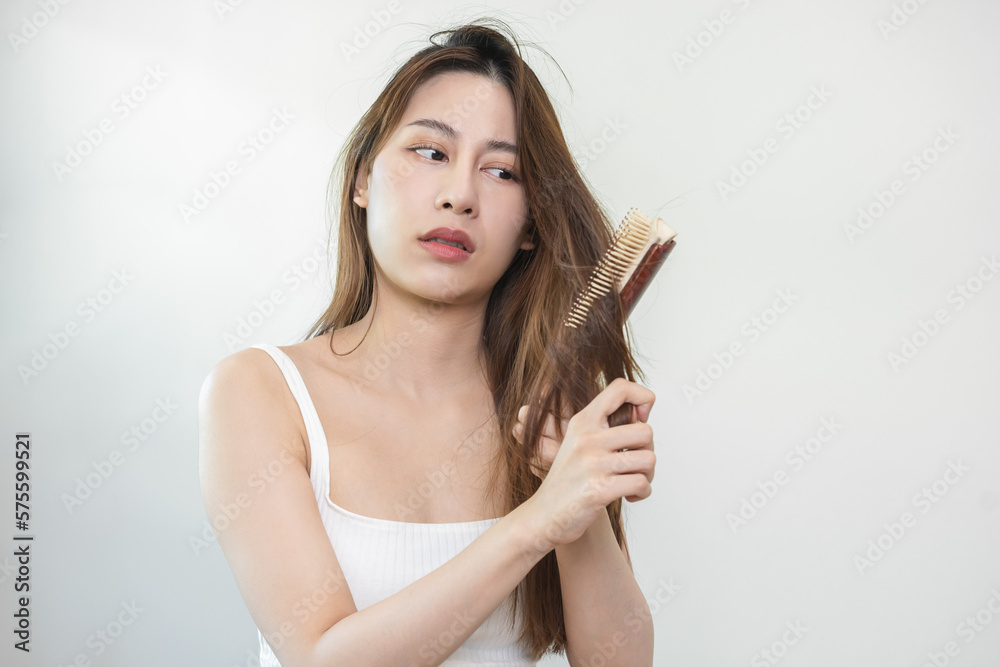 Fototapeta premium Damaged Hair, frustrated asian young woman, girl hand in holding brush splitting ends messy while combing hair, unbrushed dry long hair. Health care beauty, portrait isolated on white background.