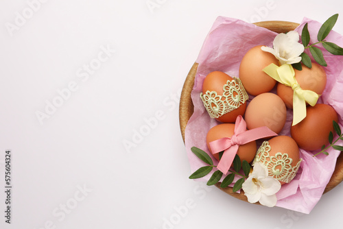 Easter eggs with colorful bows, twigs and flowers on white background, top view. Space for text