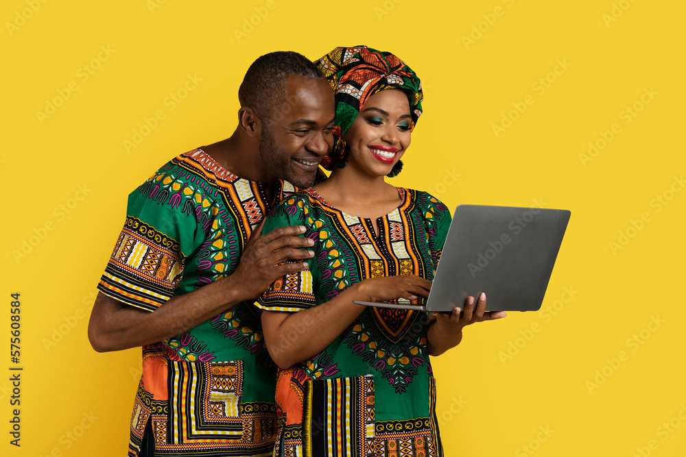 Obraz premium Beautiful black couple using modern laptop on yellow
