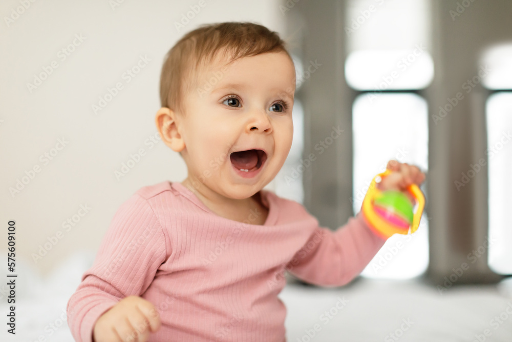 Child care concept. Portrait of pretty little girl sitting in bed with toy and smiling, adorable baby looking away at free space Child care concept. Portrait of pretty little girl sitting in bed with toy and smiling, adorable baby looking away at free space