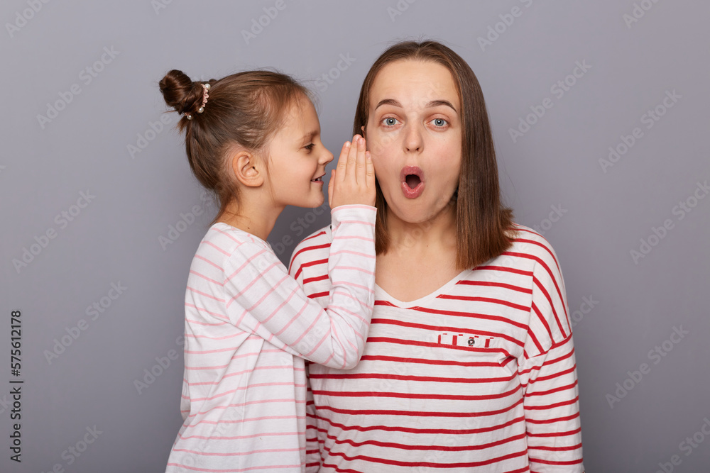 Portrait of shocked surprised mother and daughter wearing casual clothes, mommy listening kid's secrets or gossips, standing isolated over gray background. Portrait of shocked surprised mother and daughter wearing casual clothes, mommy listening kid's secrets or gossips, standing isolated over gray background.