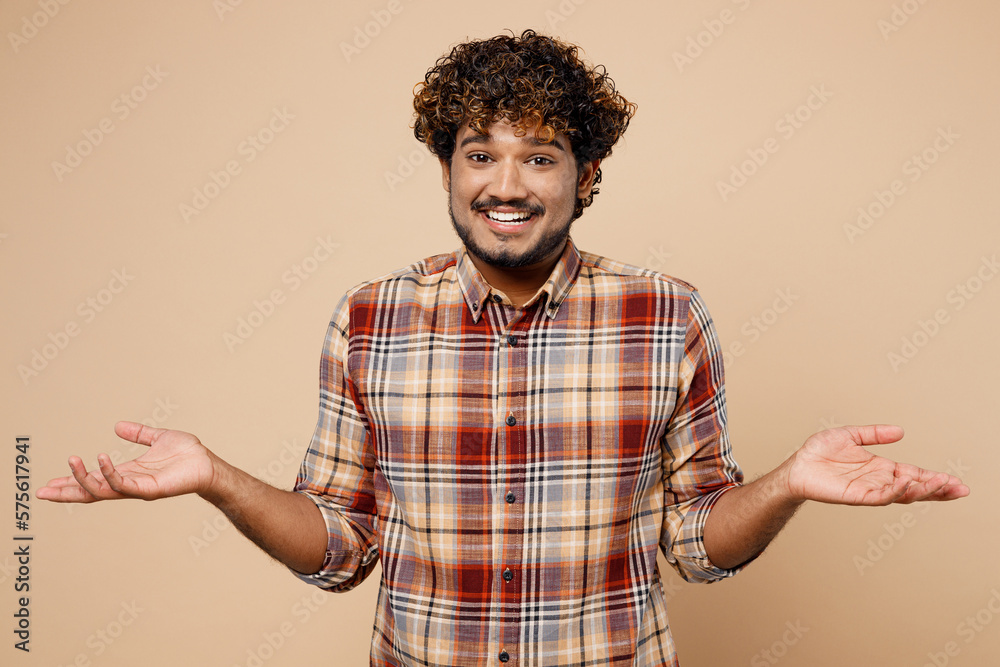 Sad Indian man wear brown shirt casual clothes shrugging shoulders looking puzzled, have no idea pread hands isolated on plain pastel light beige background studio portrait. People lifestyle concept. Sad Indian man wear brown shirt casual clothes shrugging shoulders looking puzzled, have no idea pread hands isolated on plain pastel light beige background studio portrait. People lifestyle concept.