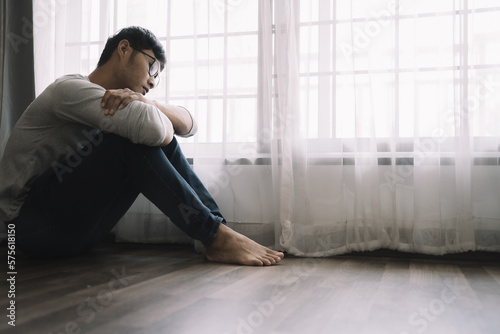 Sad and depressed young male sitting on the floor in the room, sad mood,feel tired, lonely and unhappy concept. Selective focus.