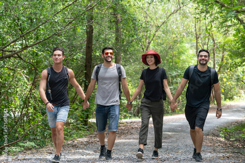 Group of happy friends with backpacks hiking together in forest. Diversity of young traveling adventure trekking with nature in holiday summer