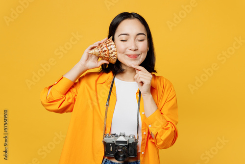 Young woman wear summer clothes hold shell near ear listen sound close eyes isolated on plain yellow background. Tourist travel abroad in free spare time rest getaway. Air flight trip journey concept. #575619510
