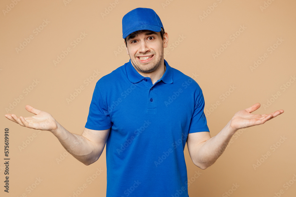 Sad delivery guy employee man wear blue cap t-shirt uniform workwear work as dealer courier spread hands shrugging shoulders looking puzzled isolated on plain light beige background. Service concept.