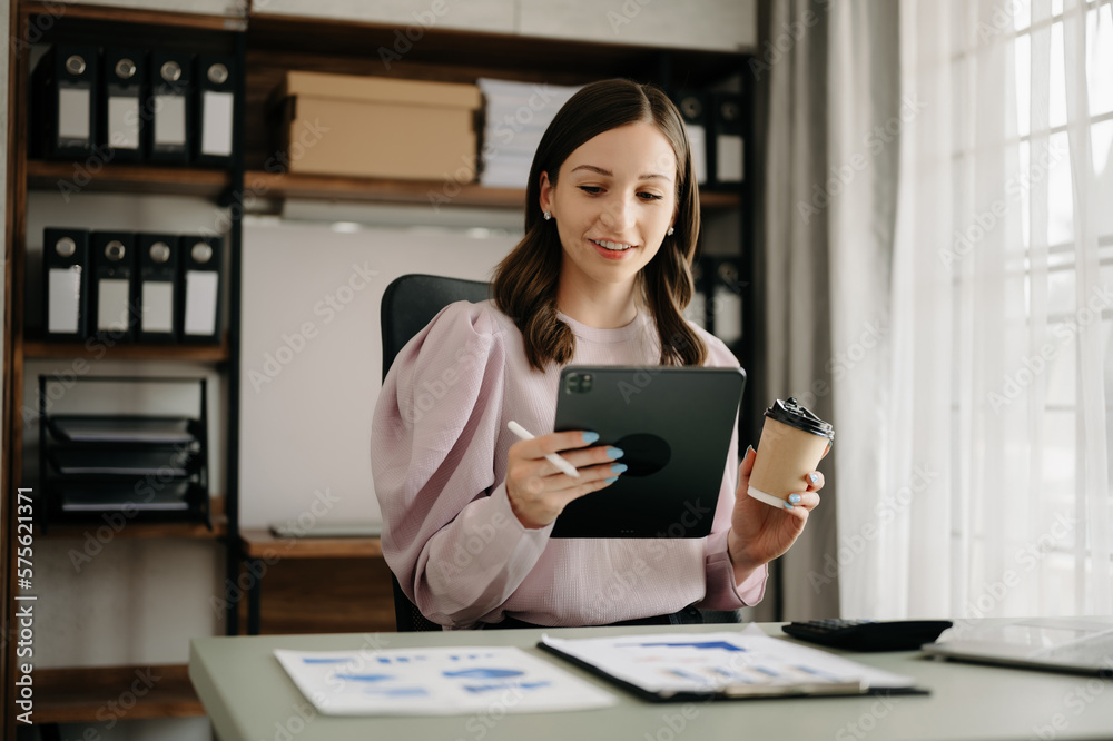 Confident business expert attractive smiling young woman typing laptop ang holding digital tablet on desk in office. Confident business expert attractive smiling young woman typing laptop ang holding digital tablet on desk in office.