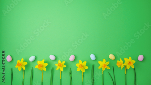 Yellow narcissus and easter eggs on green background. Spring, easter concept. Flat lay, top view, copy space