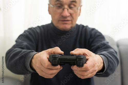 retirement elderly smile sitting on sofa life gaming, lifestyle senior old man enjoying holding joystick playing video game at home, gamer mature man hands using game controller play videogame