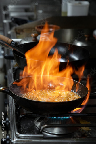 Pan on fire while flambeeing prawns for a delectable meal in a commercial kitchen, big skillet in flames while a skillful chef is cooking prawns in tasty garlic sauce for a mouthwatering seafood dish