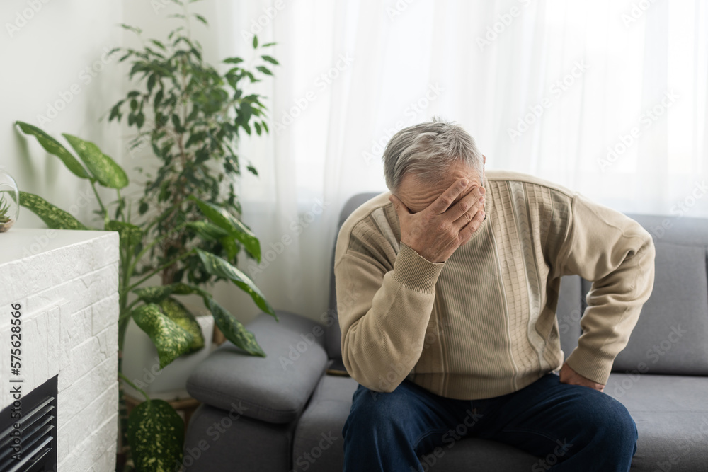 Tired old man suffering from headache, massaging his temples. Strong migraine attack. An elderly man has a headache, massaging his temples