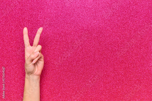 woman hand peace gesture on glitter pink background copy space