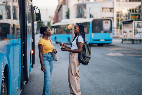 Fototapeta Couple of african american woman talking while waiting on a bus stop