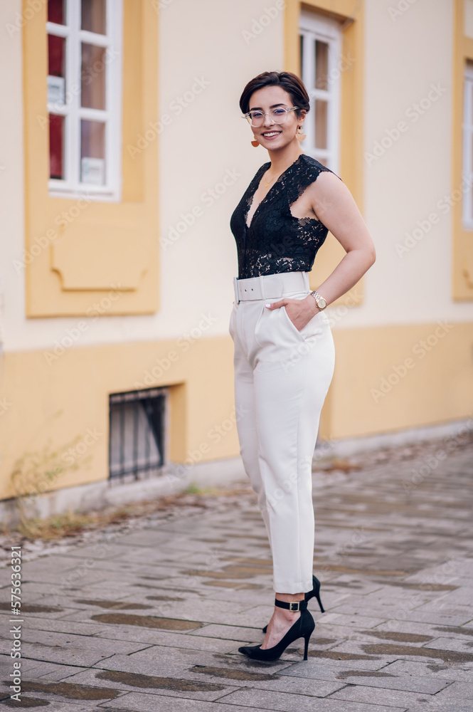 Woman wearing beige pants and a black lace top walking in the city street Woman wearing beige pants and a black lace top walking in the city street