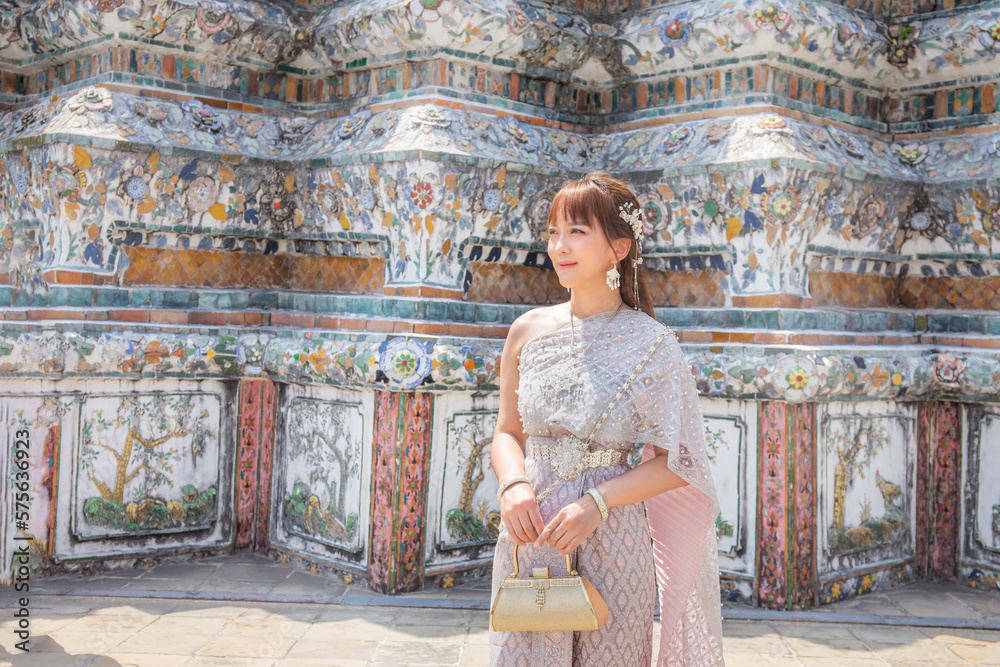 Young woman wearing Thai dress with accessories holding a bag at Wat Arun Ratchawararam It is a popular destination for tourists around the world. Bangkok, Thailand