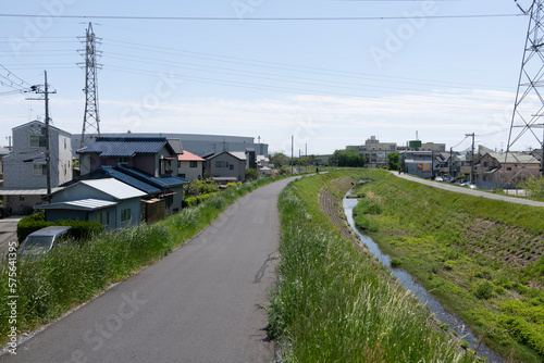 This stock photo captures a peaceful river flowing through a quiet residential neighborhood, surrounded by a beautiful blue sky and embankment.