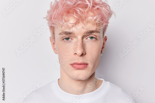Fotografiet Close up shot of serious attentive pink haired man with earring dressed casually has calm expression looks directly at camera isolated over white background has unusual appearance