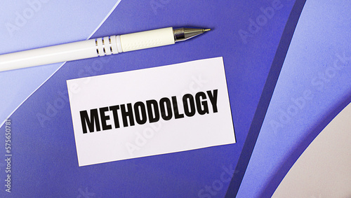 On a lilac and purple background, a white card with the text METHODOLOGY and a white pen. Layered background.