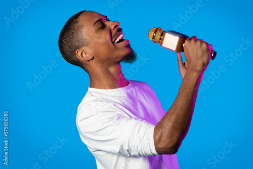 Talented young black guy singing on blue, holding microphone