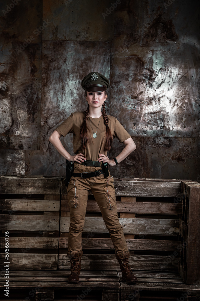 American pilot. A beautiful young woman in a uniform and with a weapon on the background of a metal wall. Staged photo. Studio light. American pilot. A beautiful young woman in a uniform and with a weapon on the background of a metal wall. Staged photo. Studio light.
