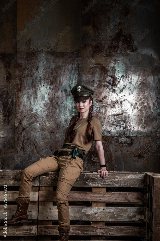 American pilot. A beautiful young woman in a uniform and with a weapon on the background of a metal wall. Staged photo. Studio light. American pilot. A beautiful young woman in a uniform and with a weapon on the background of a metal wall. Staged photo. Studio light.