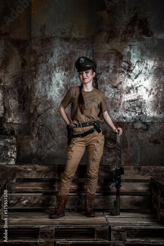 American pilot. A beautiful young woman in a uniform and with a weapon on the background of a metal wall. Staged photo. Studio light. © algrigo