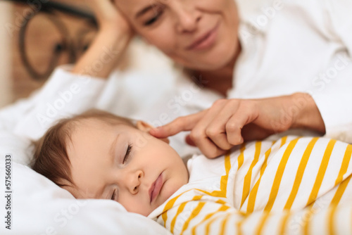 Obraz na plátně Young woman caressing her sleeping little baby girl, woman touching her kid chee