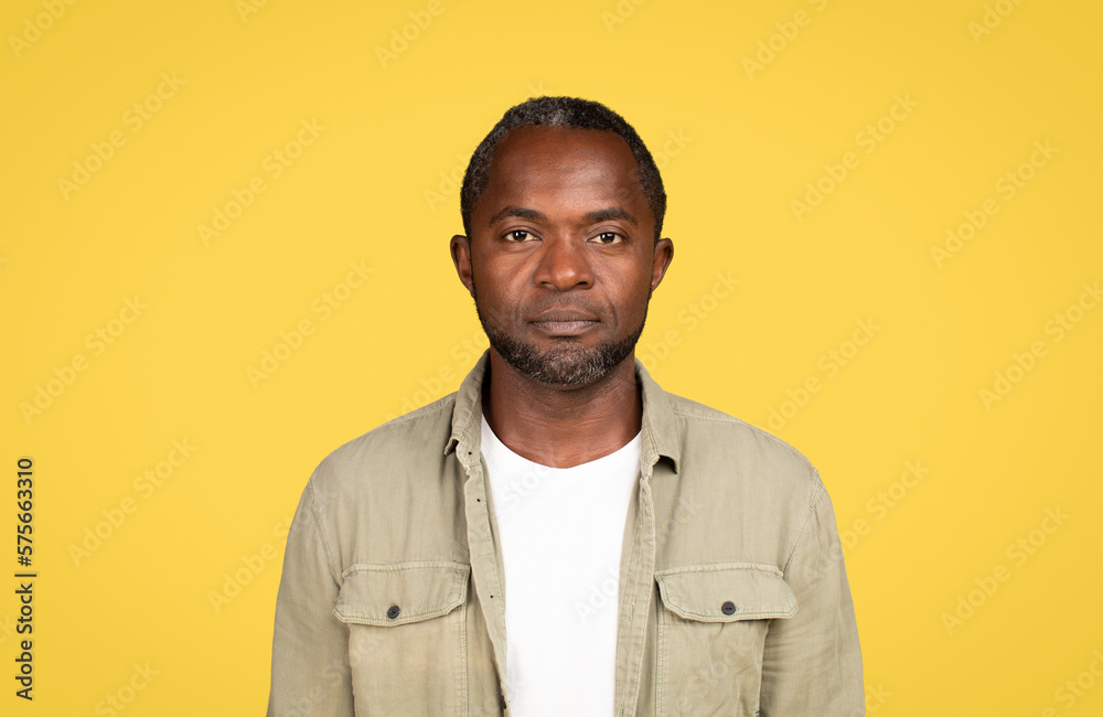 Fototapeta premium Calm serious confident mature black male in casual looking at camera, isolated on yellow background, studio