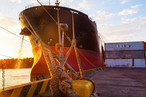A cargo ship moored to the mooring bollard of the seaport with ropes.