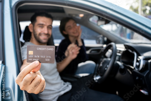 Happy smiling Caucasian couple sitting inside his new car showing credit card. Personal transportation auto purchase concept. © Chalermphon