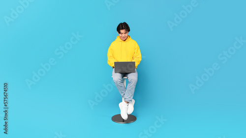 Korean Teen Guy Using Laptop Sitting Over Blue Studio Background