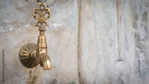 Brass faucet on a fountain with patterned marble wall, a public bronze faucet fountain in the old Ottoman traditional style. Vintage public fountain wallpaper