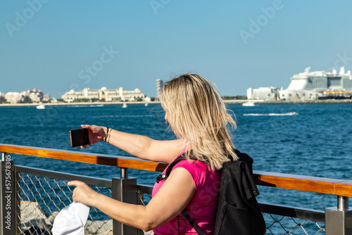 a pice of a blonde tourist girl with a rucksack standing on a Dubai embankment with a stunning view of the sea and surrounding contemporary skyscrapers