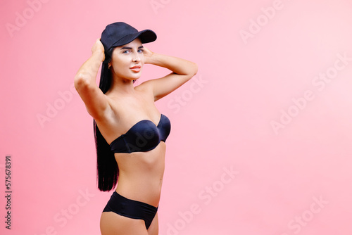 Attractive girl in a black bikini and cap standing on a pink background with a perfect body. Isolated. Studio shot.