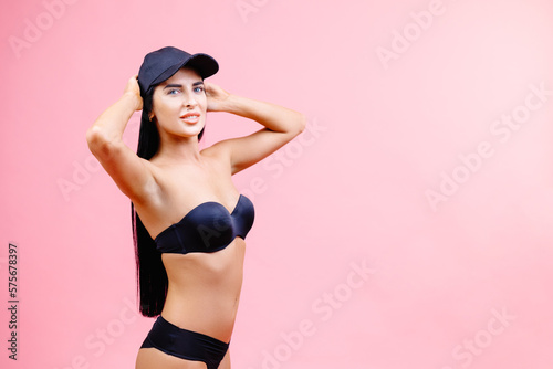 Attractive girl in a black bikini and cap standing on a pink background with a perfect body. Isolated. Studio shot.