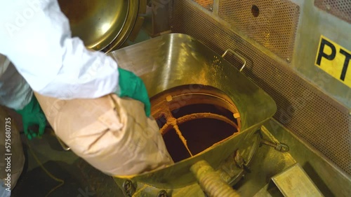 A worker at a factory pouring raw paint into production machine
