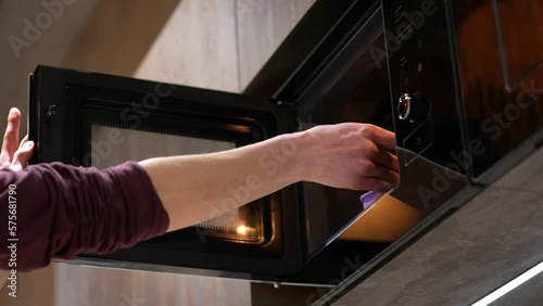 A man's hand puts a plastic container with food in the microwave. Slow motion. Concept: fast food at home, frozen food, convenience foods