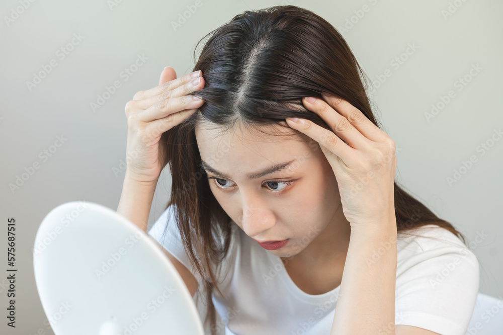 Fototapeta premium Damaged Hair, face serious asian young woman worry looking at scalp in mirror, hand in break into front hair loss, thin problem symptom at home. Health care shampoo beauty, isolated on background.