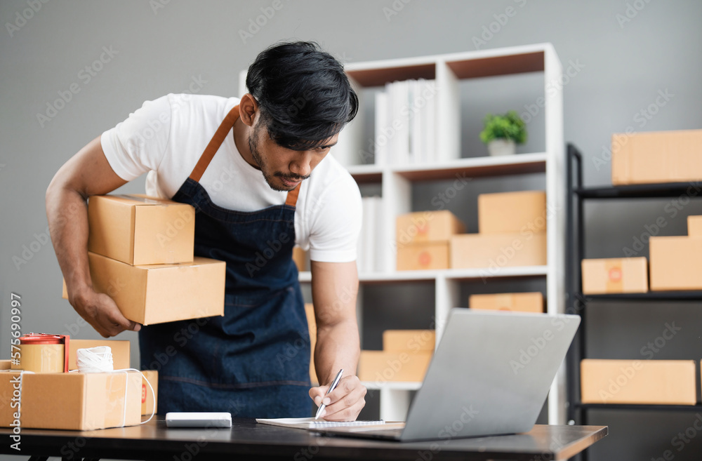 Male online store small business owner entrepreneur seller packing shipping ecommerce box checking website retail order using laptop preparing delivery parcel on table. Dropshipping concept. Closeup Male online store small business owner entrepreneur seller packing shipping ecommerce box checking website retail order using laptop preparing delivery parcel on table. Dropshipping concept. Closeup