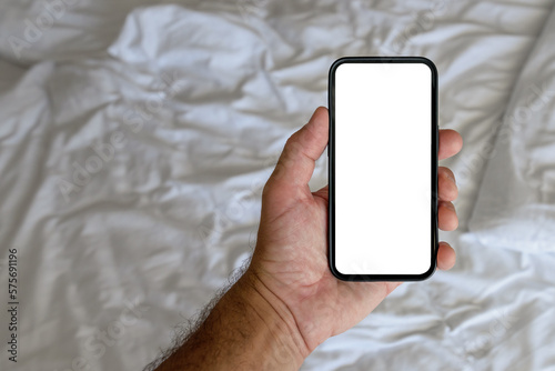 Male tourist in hotel bedroom holding smartphone with blank mockup screen for booking and reservation app or accommodation rating service