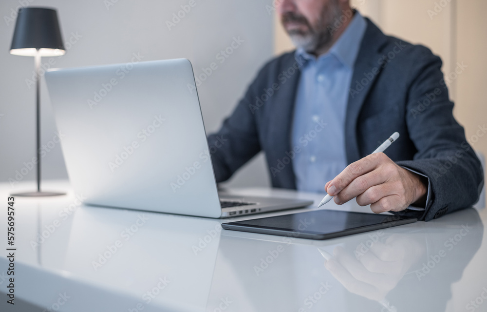 Businessman working with laptop and tablet sitting at the desk. Man write with electronic stylus pen Businessman working with laptop and tablet sitting at the desk. Man write with electronic stylus pen