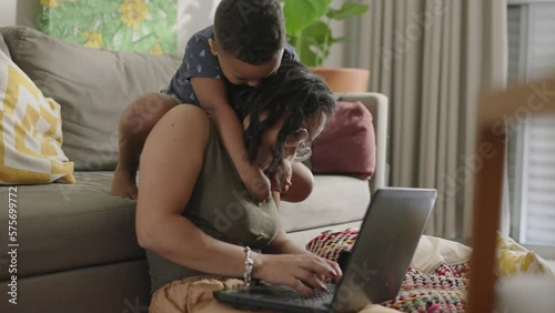 Woman working from home with laptop. Home office and parenthood at the same time. Exhausted parent with hyperactive child. Chaos with kids at home
