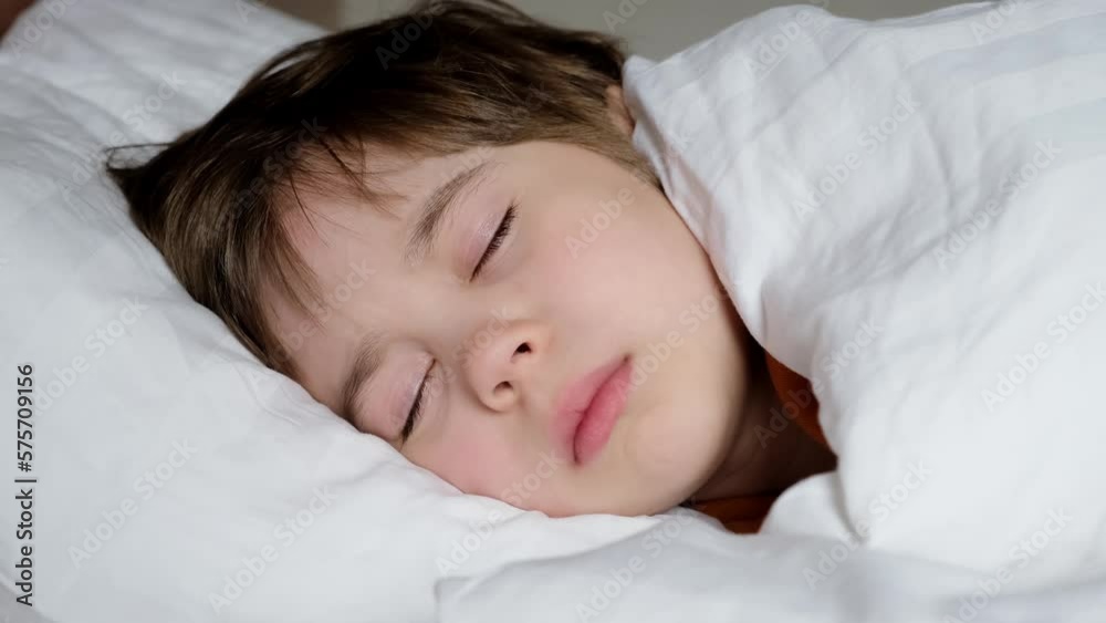 One happy boy sleeps in bed under blanket. The child at daytime relax. White linens. Dreaming time. Concept of soft and comfortable mattress and pillow. Soft pillow and warm blanket. The happy dreams. One happy boy sleeps in bed under blanket. The child at daytime relax. White linens. Dreaming time. Concept of soft and comfortable mattress and pillow. Soft pillow and warm blanket. The happy dreams.