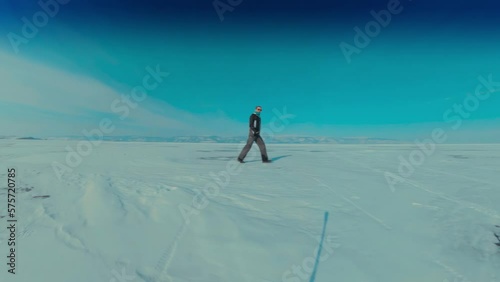 A traveler walks through a snowy wasteland on Lake Baikal wearing dark glasses in winter. A bright sunny day, a panorama