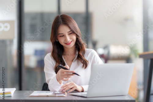 Happy Asian businesswoman sitting and working with laptop computer in office.